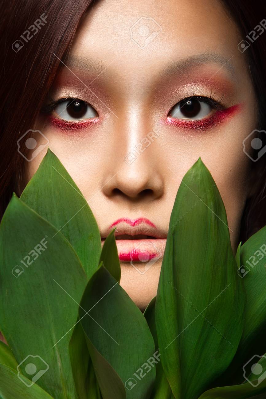 Schönes asiatisches Mädchen mit einem hellen Make-up-Kunst in grünen  Blättern. Beauty