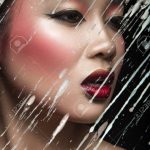 Schöne asiatische Mädchen mit hellen Make-up hinter Glas mit Tropfen Wachs.  Beauty Gesicht