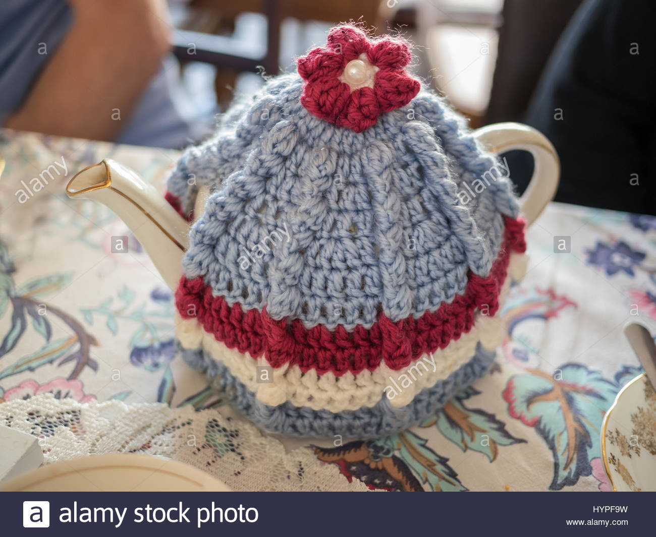 Vintage-Stil-Teekanne und gestrickter Wolle Tee gemütlich auf einer  gemusterten Tischdecke mit einer Spitzen-Matte daneben.